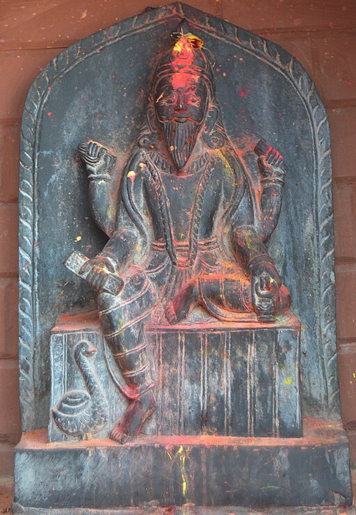 Stone statue of Vishwakarma, the celestial architect in Hindu mythology, depicted seated with tools and a swan beside him, symbolizing divine craftsmanship and creation.