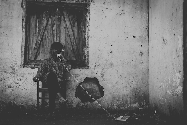 A man sits on a chair talking on a corded phone, an early symbol of remote communication in care.